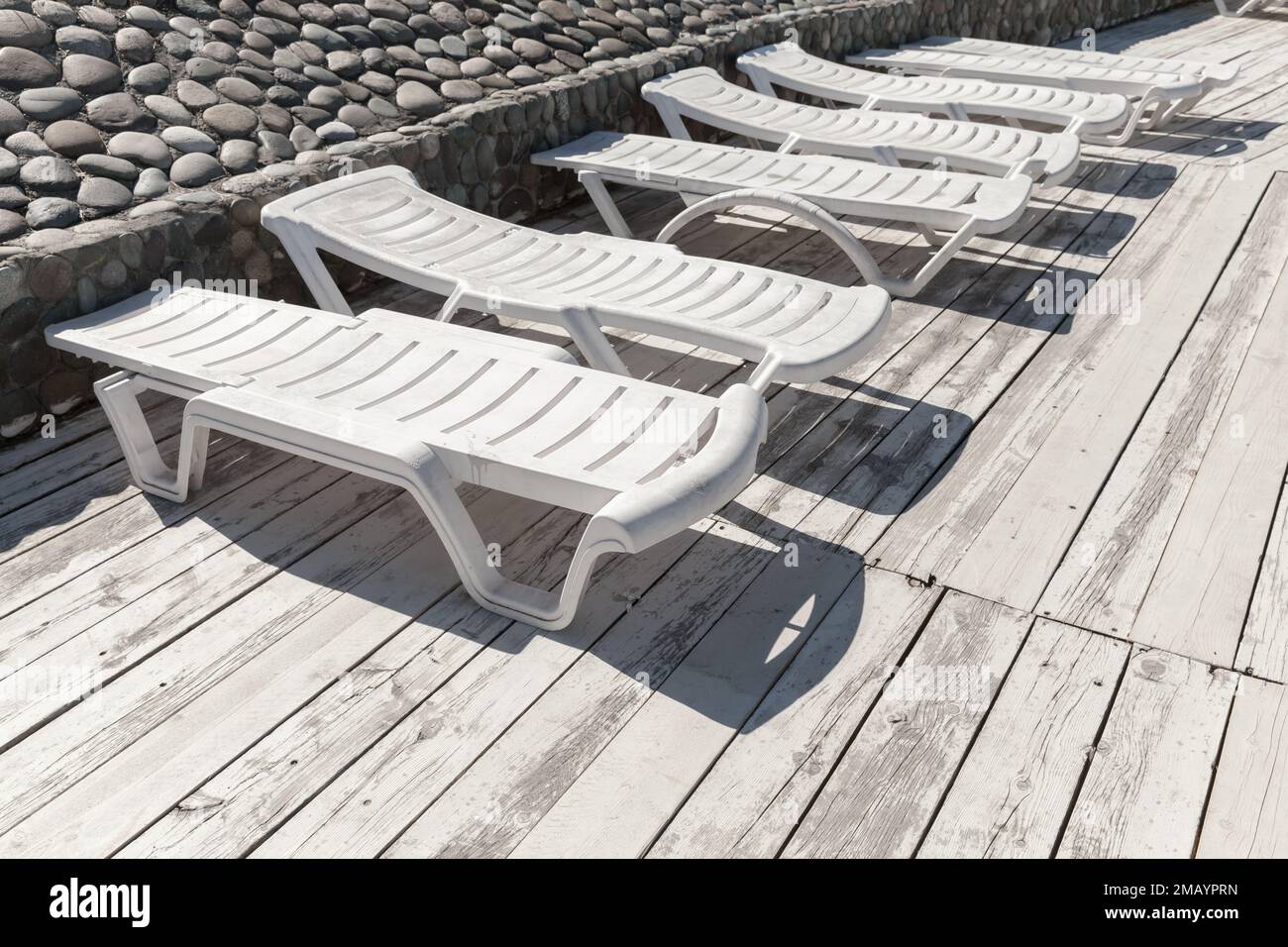 In una giornata di sole, i lettini in plastica bianca sono disponibili su una terrazza in legno Foto Stock