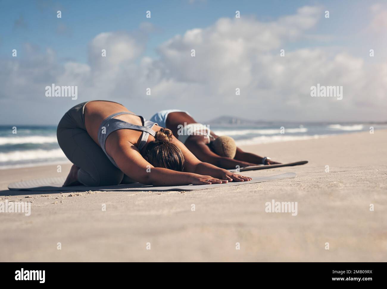 Lo yoga ci mantiene in forma fisica e mentale. due giovani donne che praticano lo yoga sulla spiaggia. Foto Stock