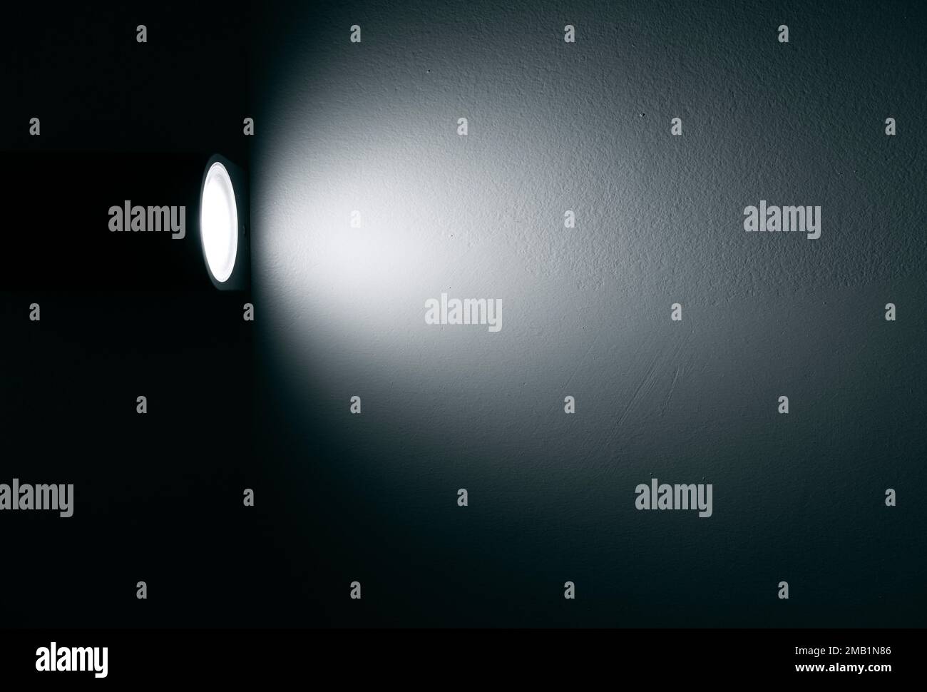 Faretto, lampada con fascio di luce sulla parete nella stanza buia Foto Stock