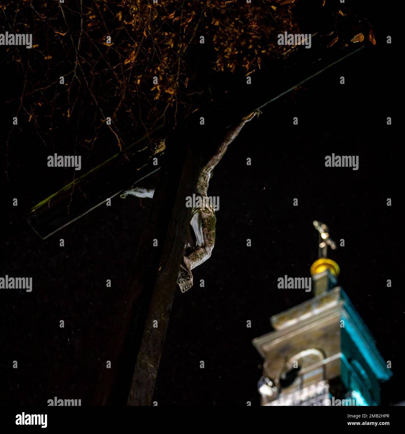 Illuminata la torre della chiesa cattolica la sera durante una nevicata pesante. Fiocchi di neve affilati in primo piano. Oggetto sfocato sullo sfondo di Foto Stock