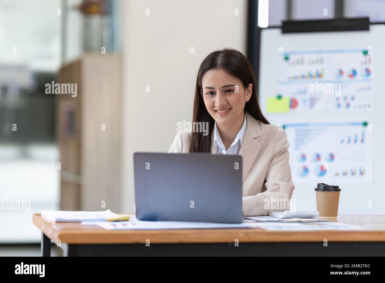 Affascinante donna asiatica d'affari che lavora su documenti finanziari, mentre si utilizza un computer portatile Foto Stock