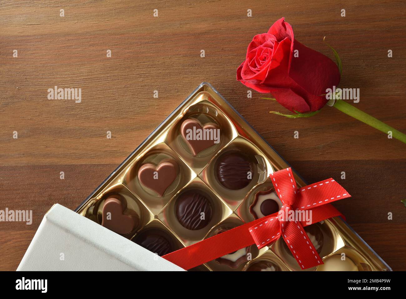 Regalo romantico con scatola assortita di cioccolatini con arco rosso e rosa su tavolo di legno. Vista dall'alto. Foto Stock