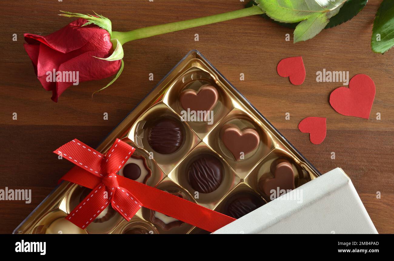 Regalo romantico con scatola assortita di cioccolatini con arco rosso e rosa con sfinestrature sul tavolo di legno. Vista dall'alto. Foto Stock