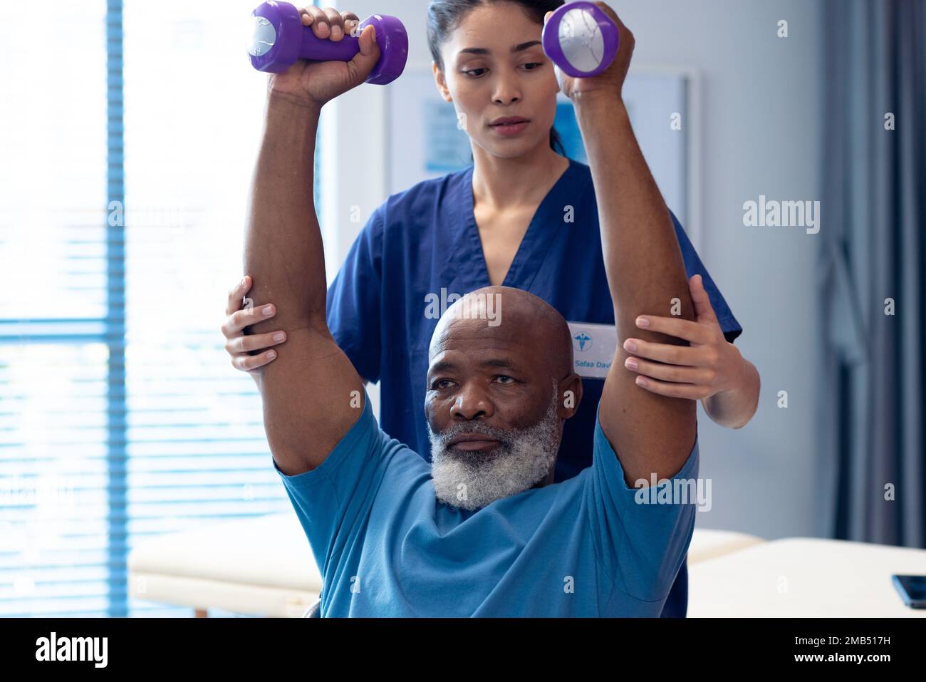 Fisioterapista femminile diversificata che aiuta il paziente anziano di sesso maschile esercizio con manubri Foto Stock