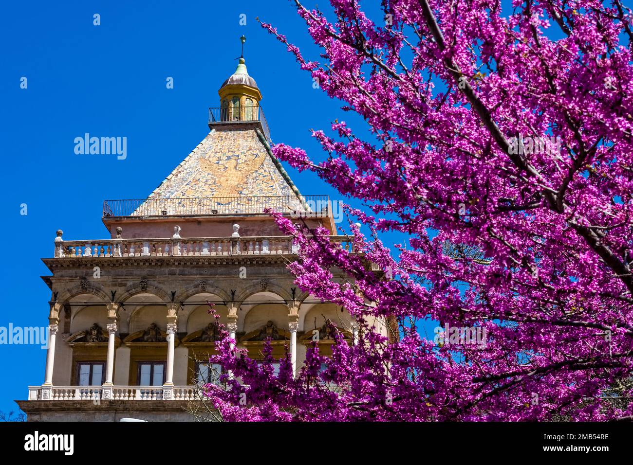 Il tetto artistico di porta Nuova, monumentale porta di Palermo, visto attraverso un albero in fiore viola. Foto Stock