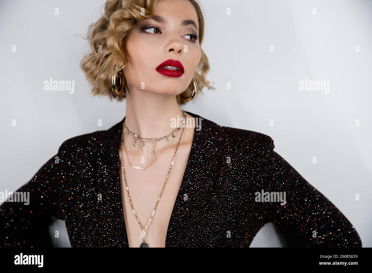 giovane donna con capelli ricci biondi e labbra rosse che si posano su grigio, immagine stock Foto Stock