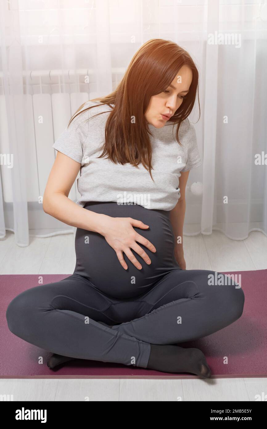 Donna incinta che tiene l'addome si accumula sul tappetino sportivo Foto Stock