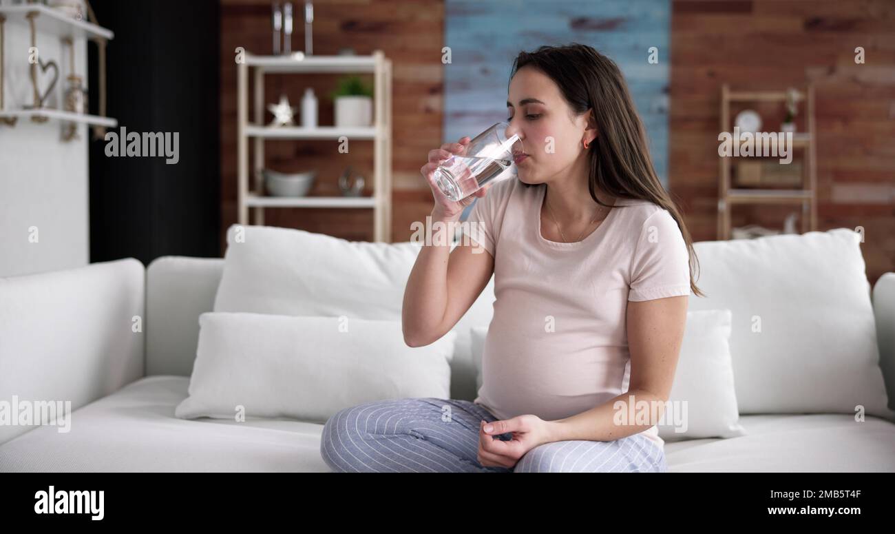 Donna incinta mano con un bicchiere di acqua e vitamina pillola Foto Stock