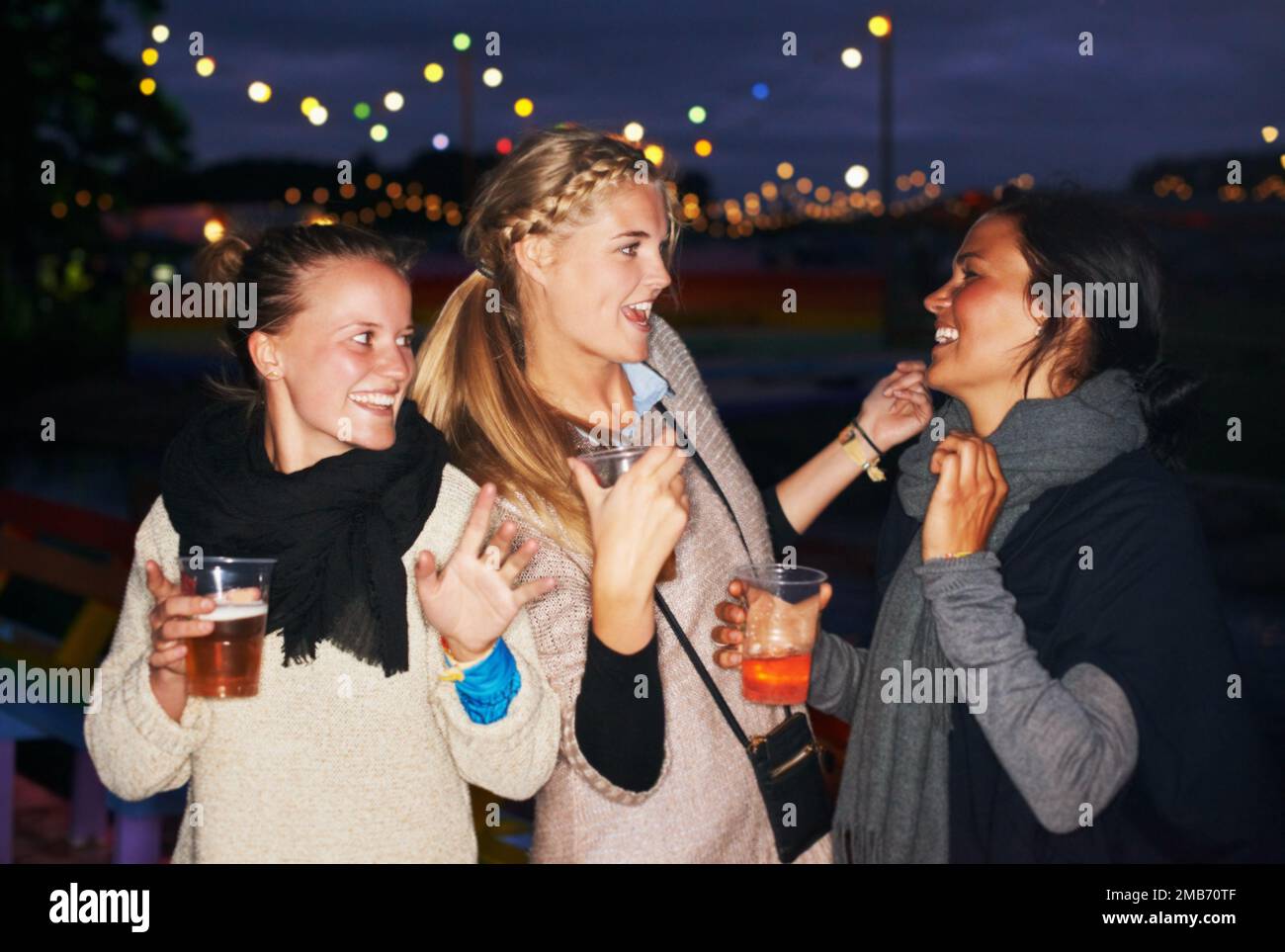 Festa sotto le stelle. tre amici che parlano e bevono di notte in un festival di musica all'aperto. Foto Stock