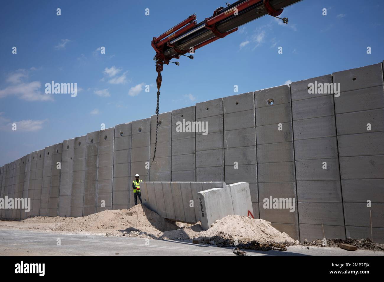 Workers place sections of a nine-meter (30-foot) high concrete wall to replace a border fence between the northern West Bank and Israel, near the Arab village of Salem, Wednesday, June 22, 2022. The Israeli defense ministry said Wednesday that it had started construction on a section of separation barrier in the northern West Bank after months of military raids in the area following a string of deadly attacks on Israelis by Palestinians. The ministry announced that it began work on a 45-kilometer (28 mile) stretch of wall to replace fencing installed 20 years earlier. (AP Photo/Ariel Schalit) Foto Stock