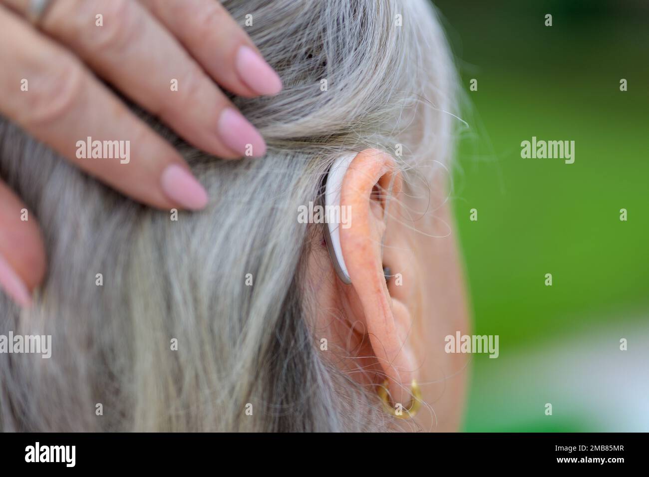 L'anziano grigio ha pelo duro della signora udente in suoi 80's pennelles i suoi capelli al lato per mostrare il suo dispositivo uditivo nel suo orecchio Foto Stock