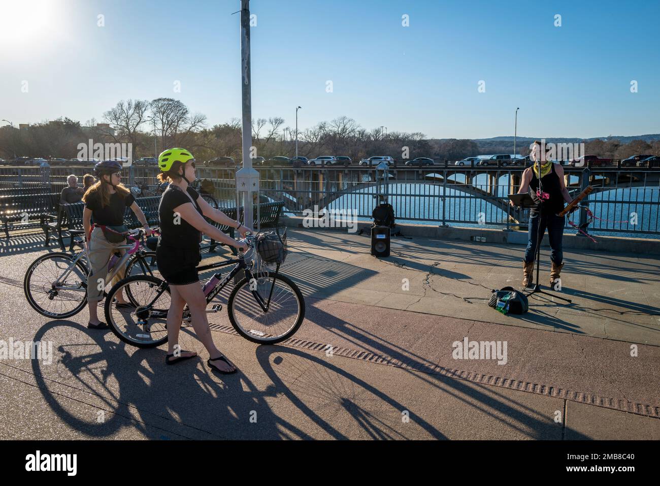 I ciclisti si fermano per ascoltare il musicista di strada sul ponte pedonale James D. Pfluger sul lago Ladybird, Austin, Texas Foto Stock
