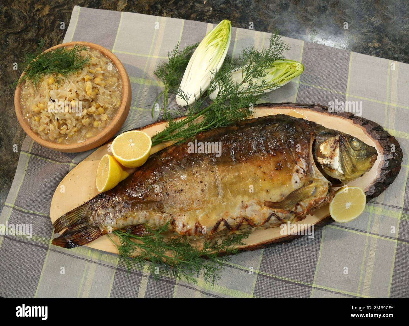 Carpa arrosto ripiena servita con fettine di limone, piselli con cavolo e aneto. Foto Stock