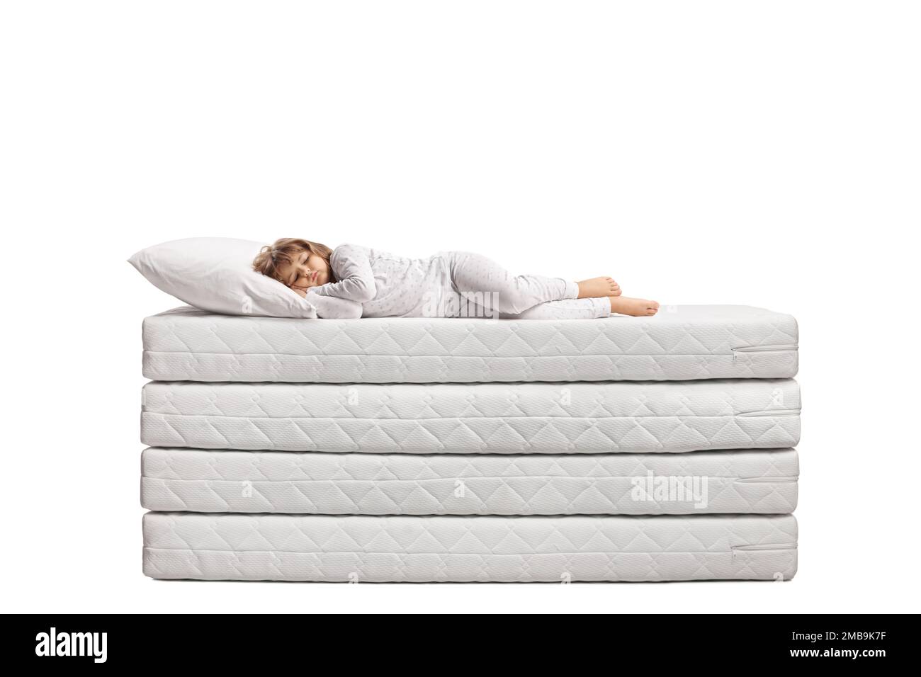 Bambina in pigiama che dorme su un mucchio di materassi isolati su sfondo bianco Foto Stock
