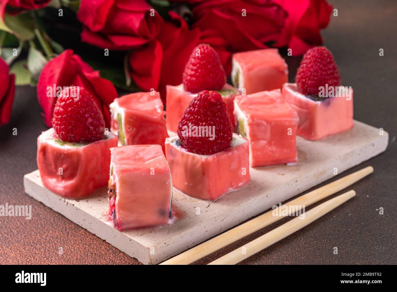 Sushi a base di frutta dolce per cena di San Valentino o brunch. Mousse bacche bianco cioccolato dolce cremoso sushi dessert, con bouquet di fiori di rosa Foto Stock