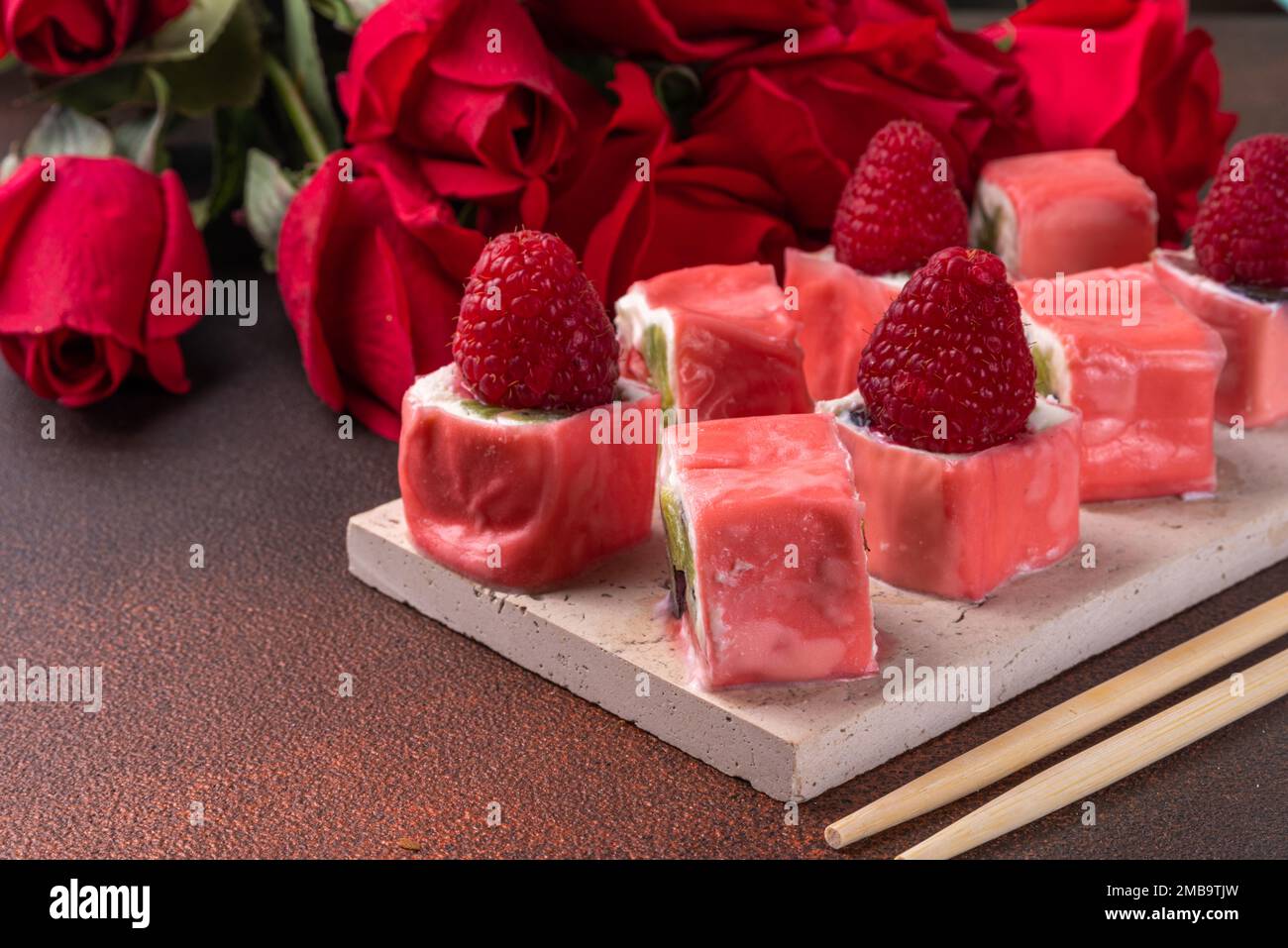 Sushi a base di frutta dolce per cena di San Valentino o brunch. Mousse bacche bianco cioccolato dolce cremoso sushi dessert, con bouquet di fiori di rosa Foto Stock