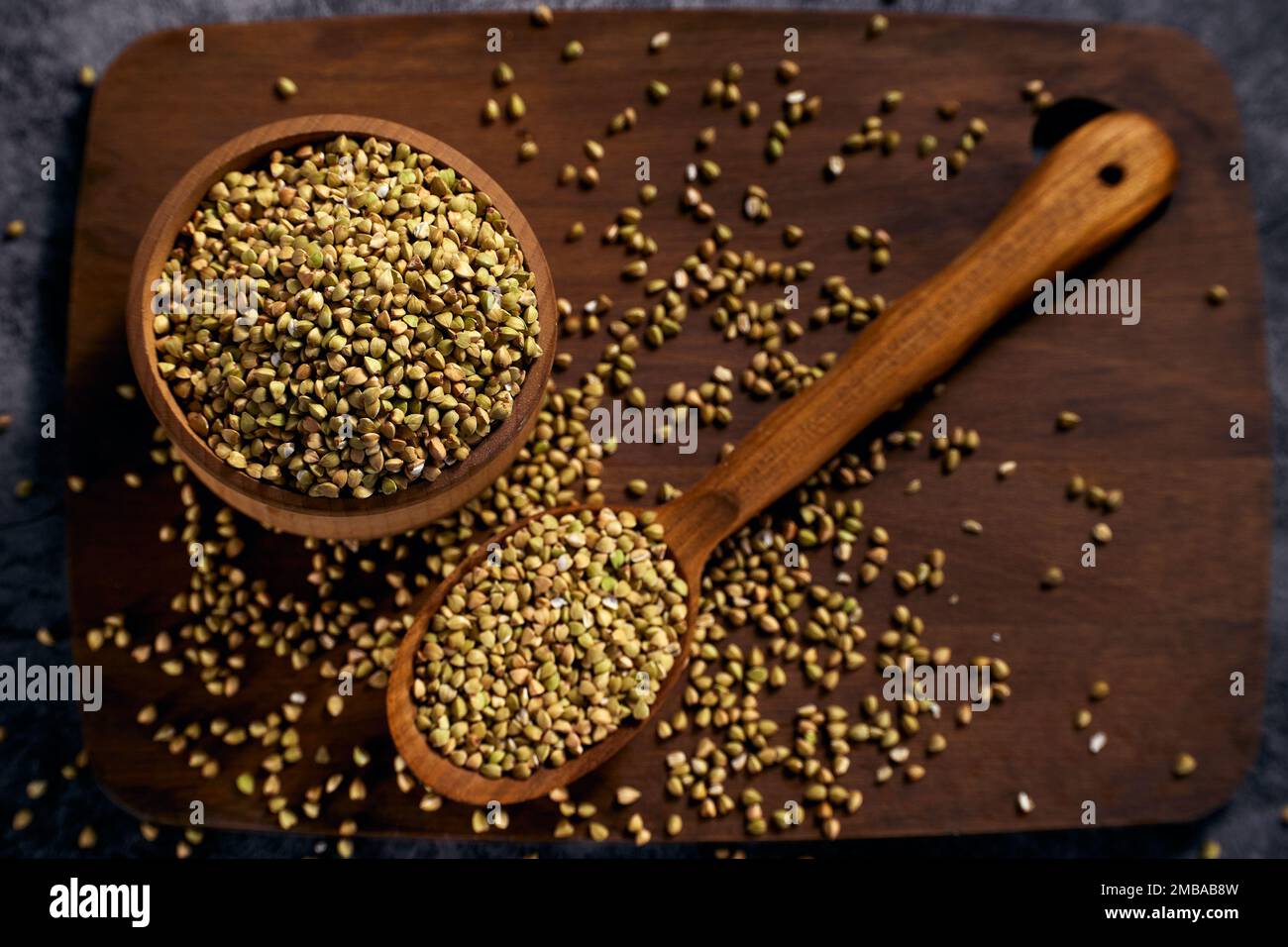 Vista dall'alto la ciotola di legno con grano saraceno verde non lavorato su tavola di legno con un cucchiaio di legno accanto ad essa Foto Stock
