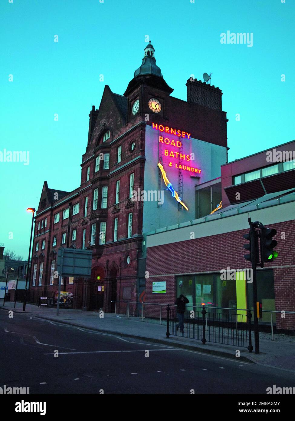 Hornsey Road Baths, Hornsey Road, Finsbury Park, Islington, Greater London Authority, 2012. Il blocco d'ingresso delle ex Hornsey Road Baths, Islington, visto da sud al crepuscolo, che mostra il segno del nome illuminato al neon e la figura di una donna subacquea all'altezza sud. I bagni di Hornsey Road furono costruiti nel 1892 e chiusi nel 1991. Le piscine sono state demolite e il sito è stato riprogettato come Tiltman Place, con blocchi di appartamenti. Il blocco d'ingresso (o casetta) e gli edifici di lavanderia sono stati convertiti in appartamenti noti come la casa di guardia. Il segno al neon di una donna subacquea a sud Foto Stock