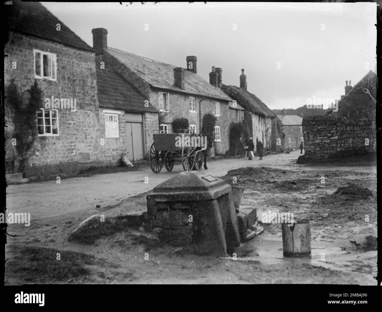 Brook Street, Shipton Gorge, West Dorset, Dorset, 1922. Una vista che guarda ad est lungo Brook Street, che mostra un carrello trainato da cavalli e cottage sullo sfondo e un secchio accanto a un villaggio ben in primo piano. Foto Stock