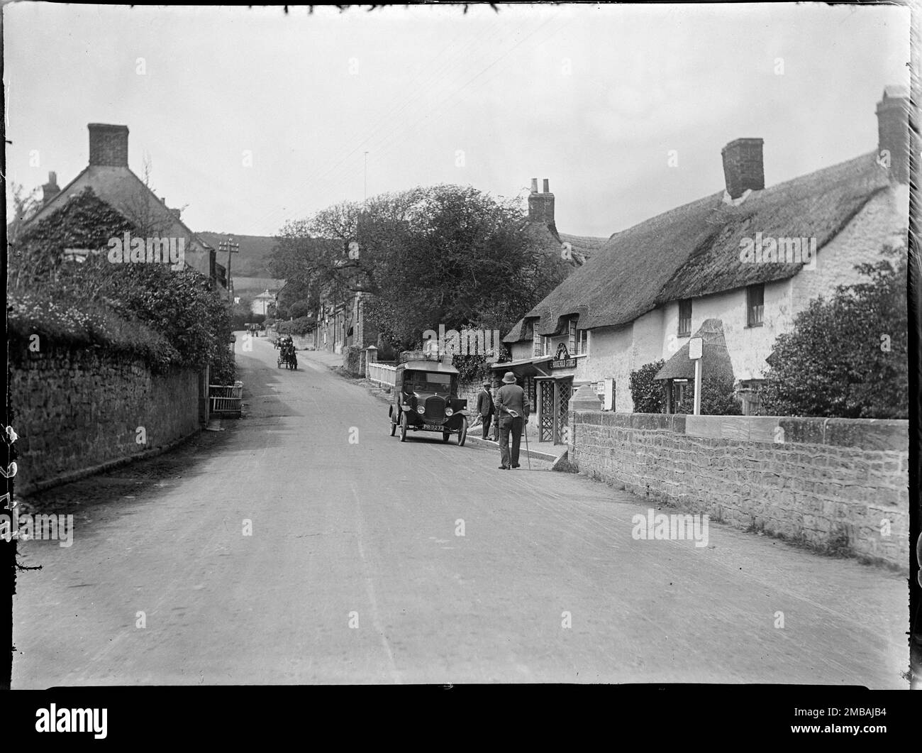 Main Street, Chideock, West Dorset, Dorset, 1925. Guardando verso ovest lungo Main Street dal ponte sul fiume Winniford, mostrando due figure e un furgone fuori dai locali di Holgate Household Stores al Bridge Cottage. Foto Stock