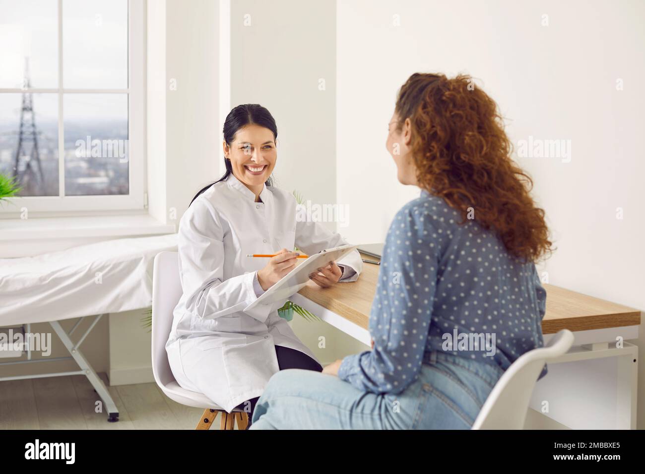 Allegro medico femminile ridendo mentre si parla con la donna mentre si riempie la sua scheda medica. Foto Stock