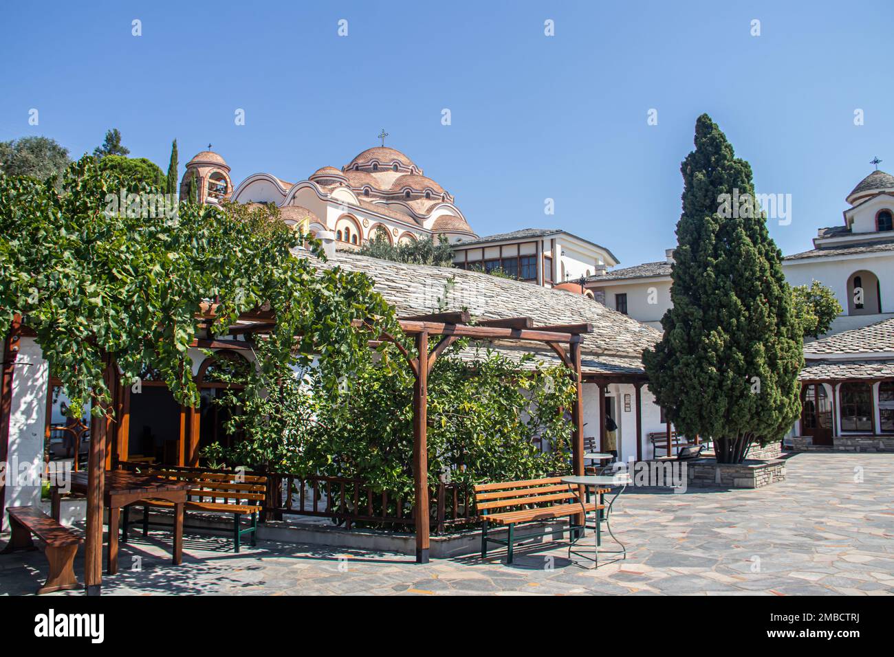 Vista sul cortile posteriore del Monastero dell'Arcangelo Michele in Grecia, l'isola di Thasos, con pareti e tetto di color arancio vivace e massicce campane della Chiesa Foto Stock