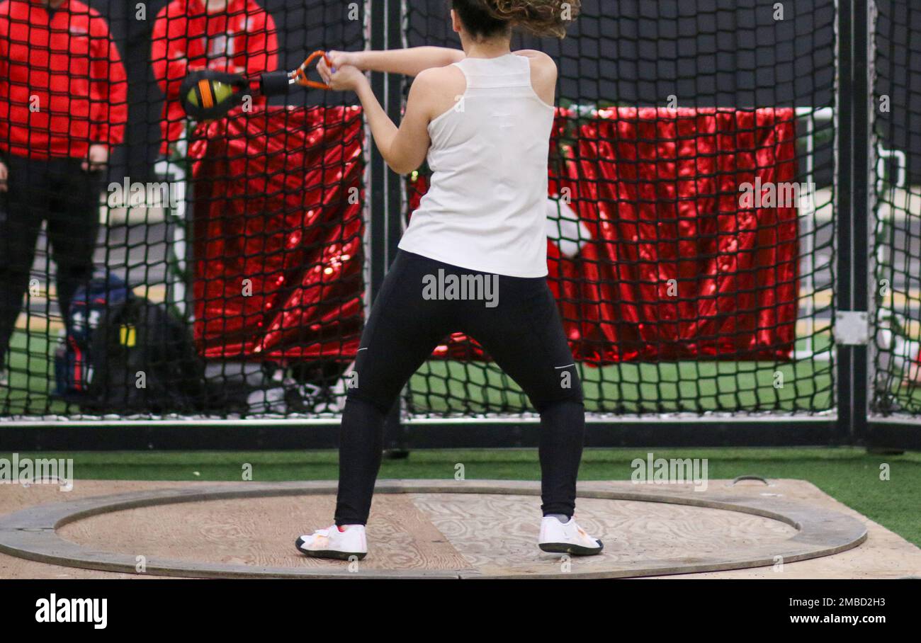 Vista posteriore di una pista femminile di scuola superiore e atleta sul campo che getta il peso durante una competizione indoor. Foto Stock
