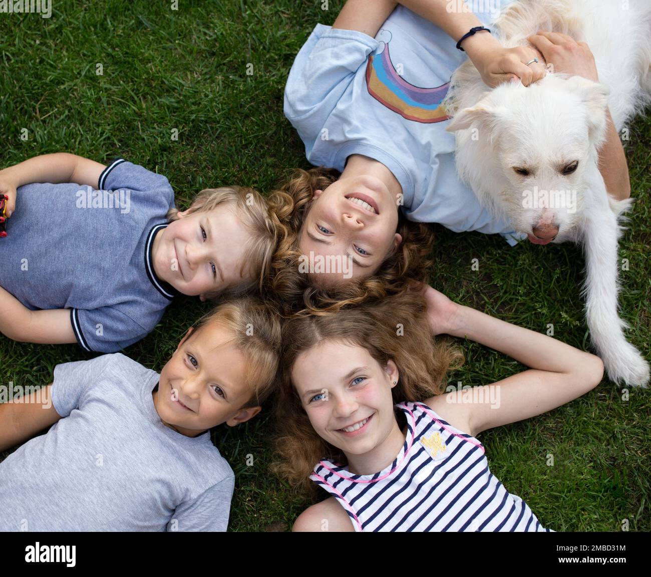 Bambini felici, ragazzi e ragazze di diverse età, sdraiati sull'erba in estate, vista dall'alto. fratelli, sorelle e cani sorridenti godono la vita, divertirsi insieme Foto Stock