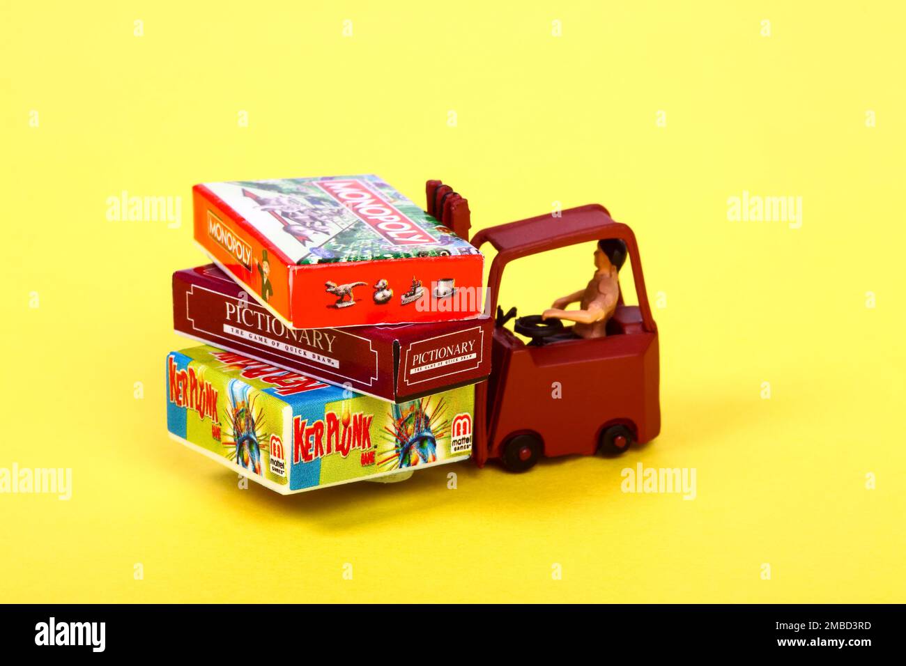 Figura in miniatura che guida un carrello elevatore impilato con i giochi da tavolo popolari Foto Stock