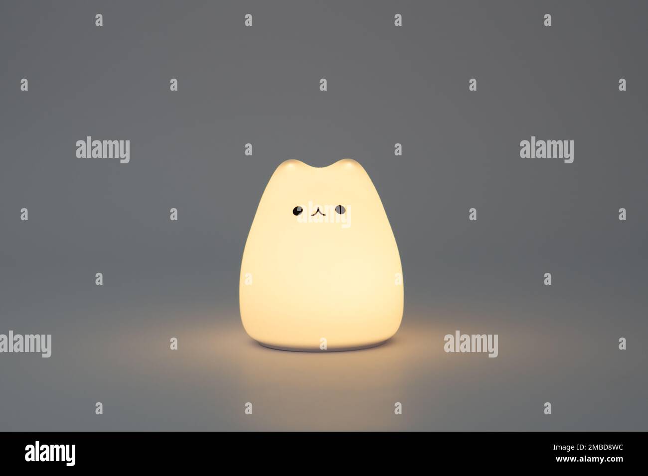 Lampada a forma di gatto su sfondo scuro. Graziosa lampada da notte in silicone a forma di gatto su sfondo bianco in uno spazio scuro. Foto Stock