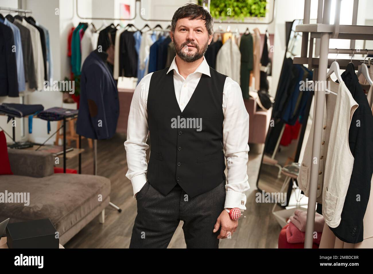 Elegante vestiario in piedi in officina tra scaffali di abbigliamento Foto Stock