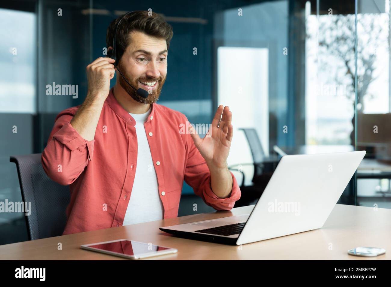 Uomo d'affari maturo di successo con cuffie per videochiamate che lavorano all'interno dell'ufficio, un uomo che si occupa di consulenza online con i clienti, che parla con i colleghi durante una riunione remota online, che si siede sul posto di lavoro con un computer portatile. Foto Stock