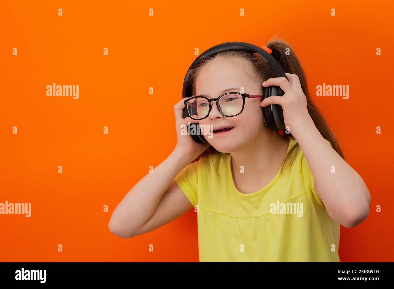 Ragazza con sindrome di Down ascolta la musica. Sfondo arancione Foto Stock