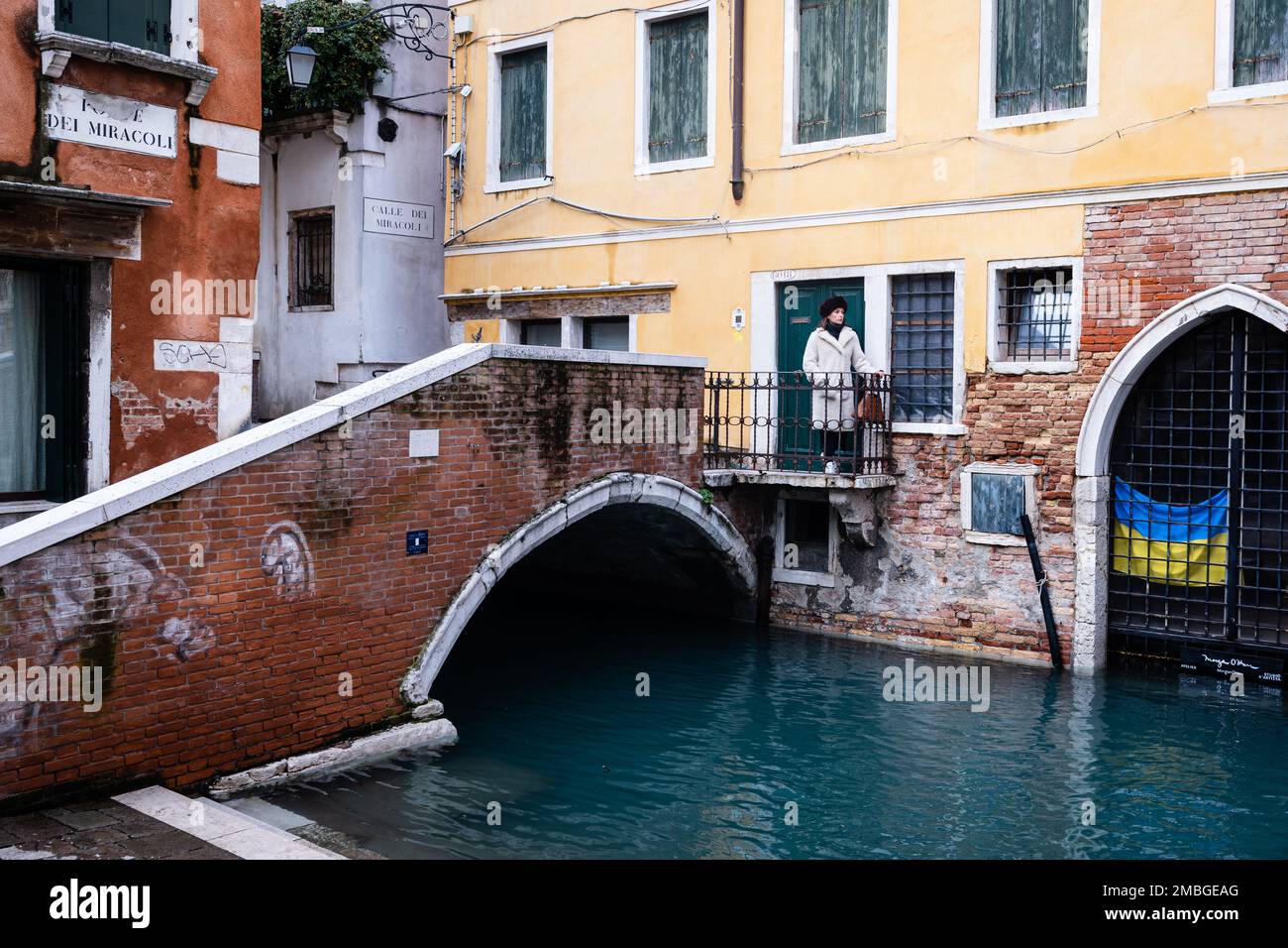 21 gennaio 2023. Ponte dei Miracoli, Venezia. Una bella donna in un cappello russo su un ponte in una Venezia deserta guarda giù su una bandiera Ucraina. Foto Stock
