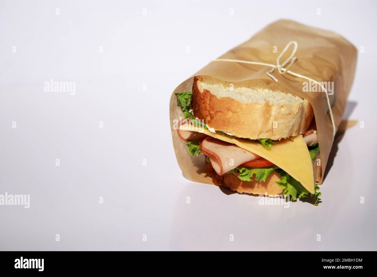 Panino di formaggio e prosciutto avvolto in carta su sfondo bianco con spazio copia Foto Stock