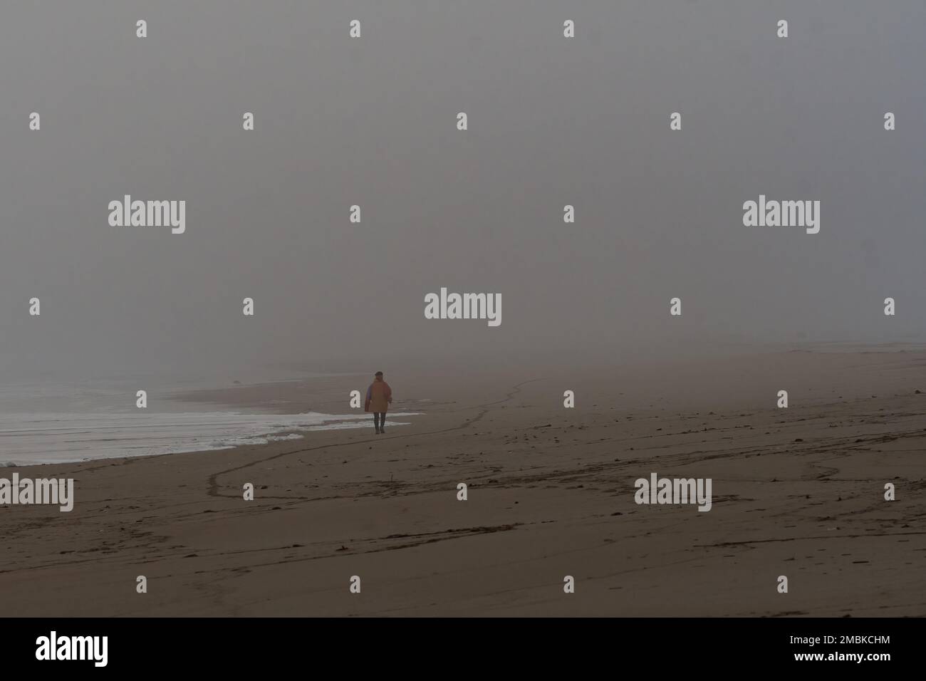 Persona sola che cammina su una spiaggia nebbiosa. Foto Stock