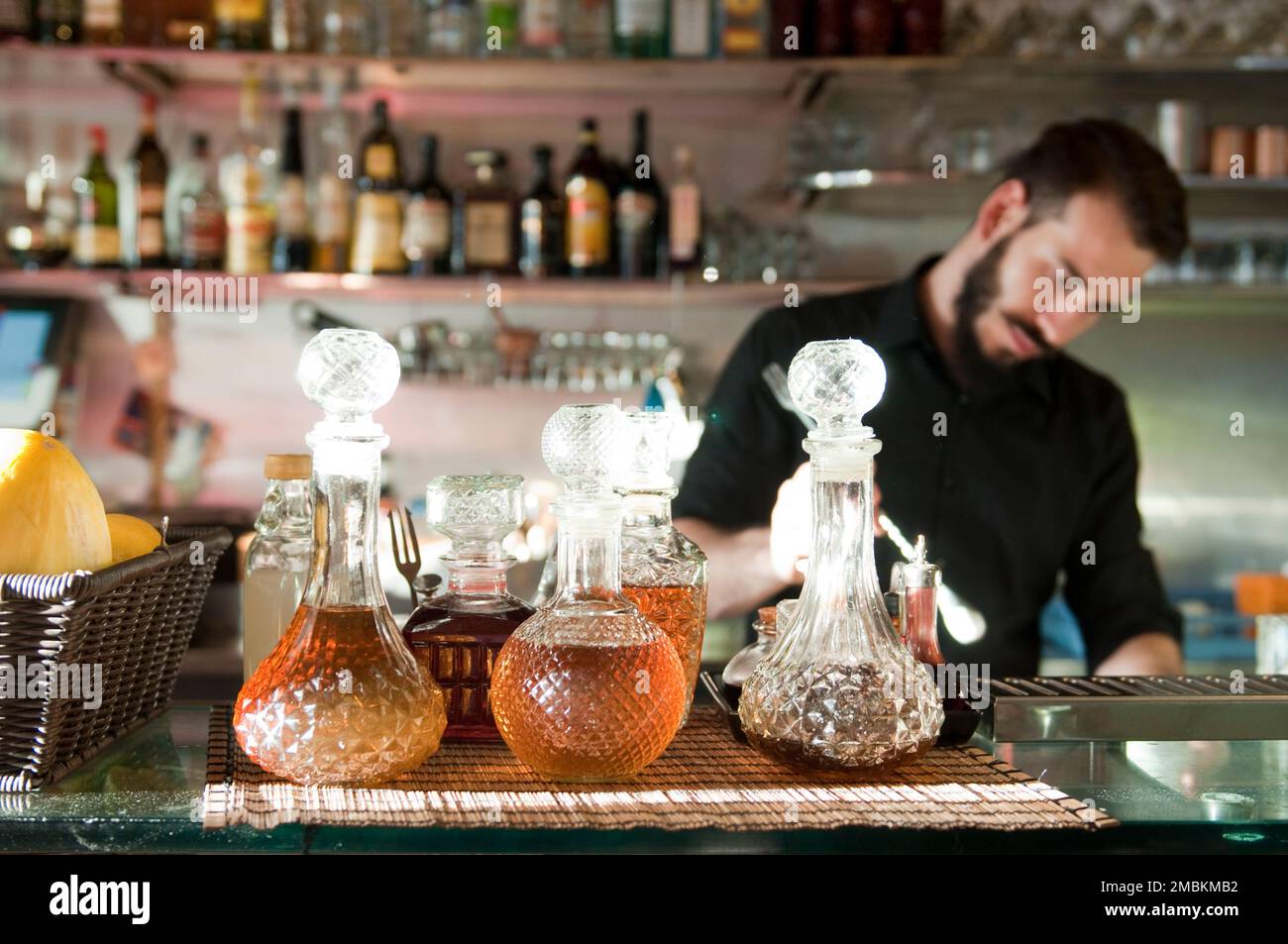 Una varietà di liquori in splendidi decanter di vetro tagliato attendono gli ospiti mentre un barista mescola un drink a Roma, in Italia. Foto Stock