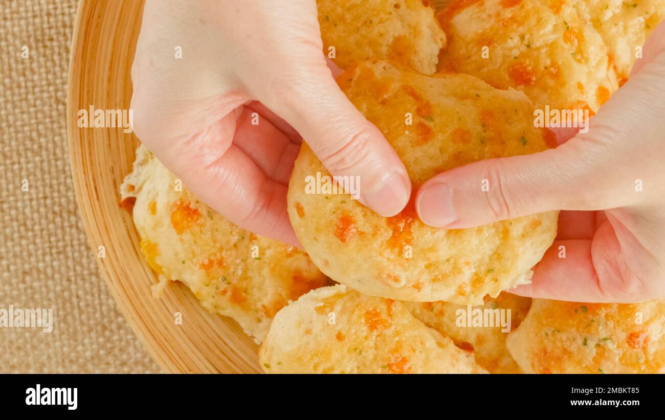 Biscotti al formaggio con burro e aglio condimento primo piano su un piatto di legno, vista dall'alto, mani di donna Foto Stock