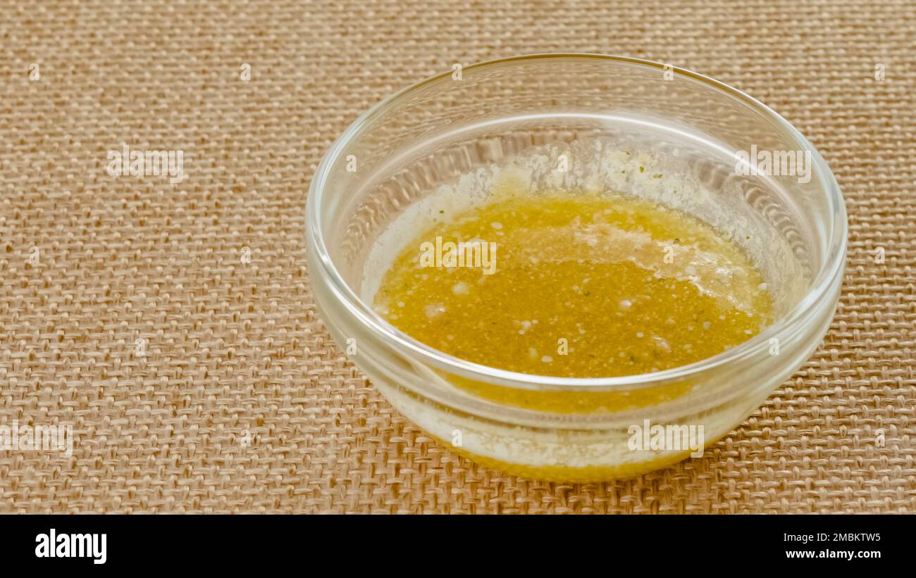 Mix di burro fuso e aglio condimento primo piano in una ciotola di vetro su un tavolo da cucina in sfondo rustico, spazio copia Foto Stock