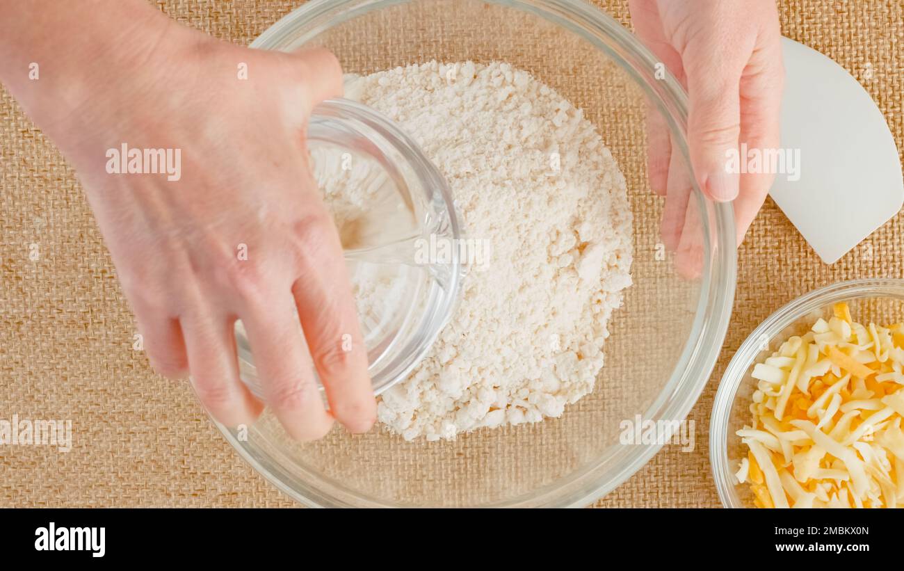 Ricetta di biscotti cheesy. Donna che mescola gli ingredienti in una ciotola di vetro, vista ravvicinata, disposizione piatta Foto Stock