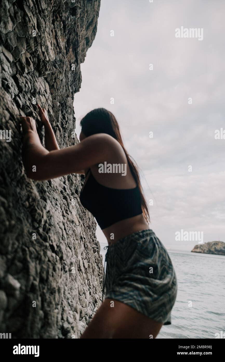 Sport Donna arrampicata sulla roccia. Giovane donna con corpo slim-fit arrampicata in grotta vulcanica basalto con bella vista mare. La ragazza atleta si allena Foto Stock