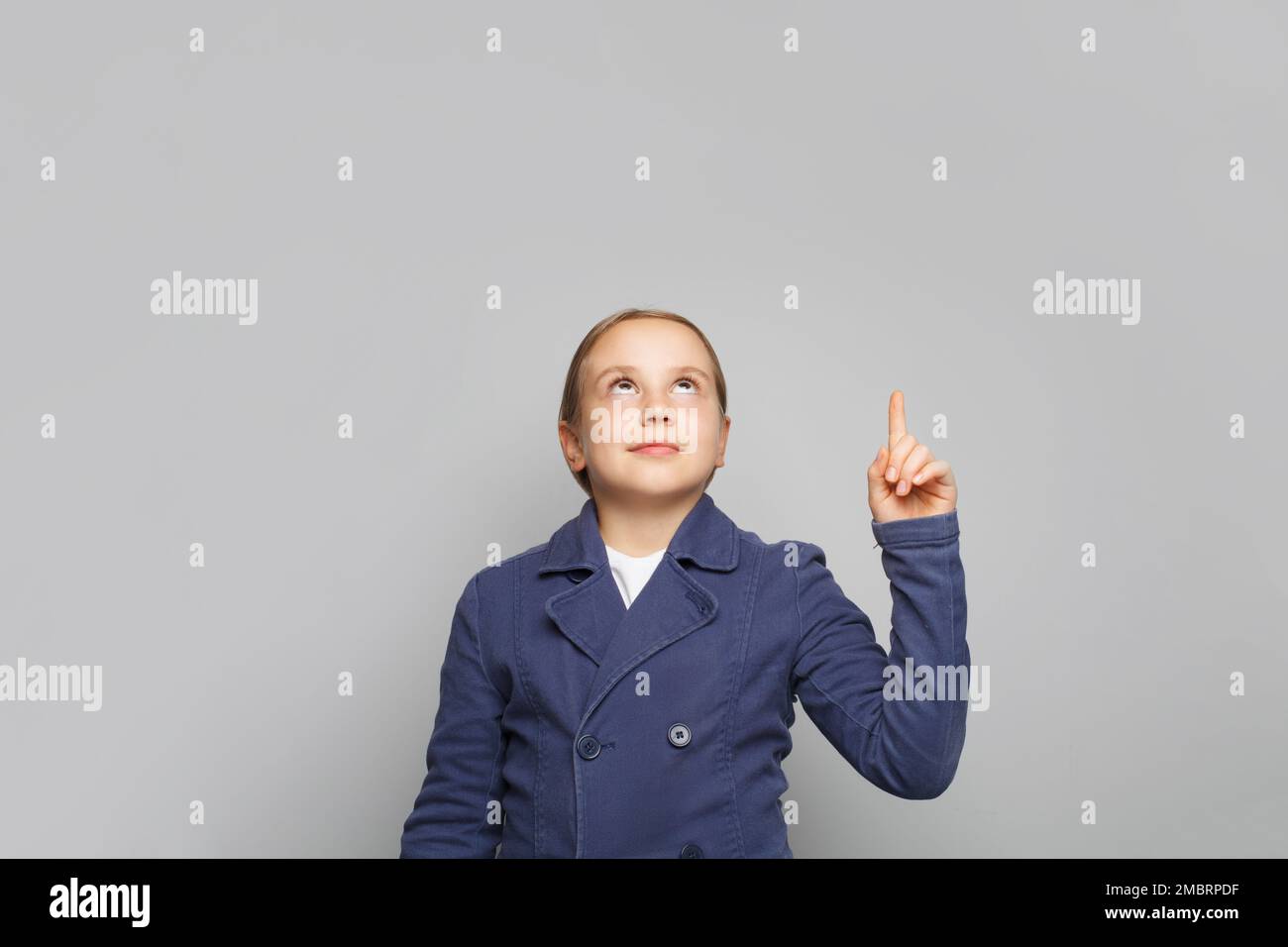 Ragazza bambino intelligente in uniforme scuola che punta e guardando su sfondo grigio banner Foto Stock