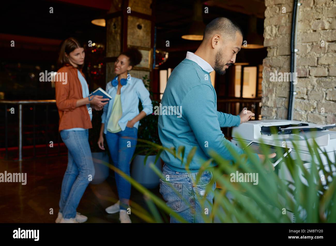 Giovane dipendente che lavora su una copiatrice presso un ufficio di coworking Foto Stock
