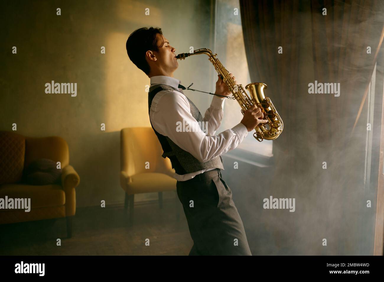 Giovane uomo elegante che suona il sassofono dell'alto in una stanza misteriosa Foto Stock