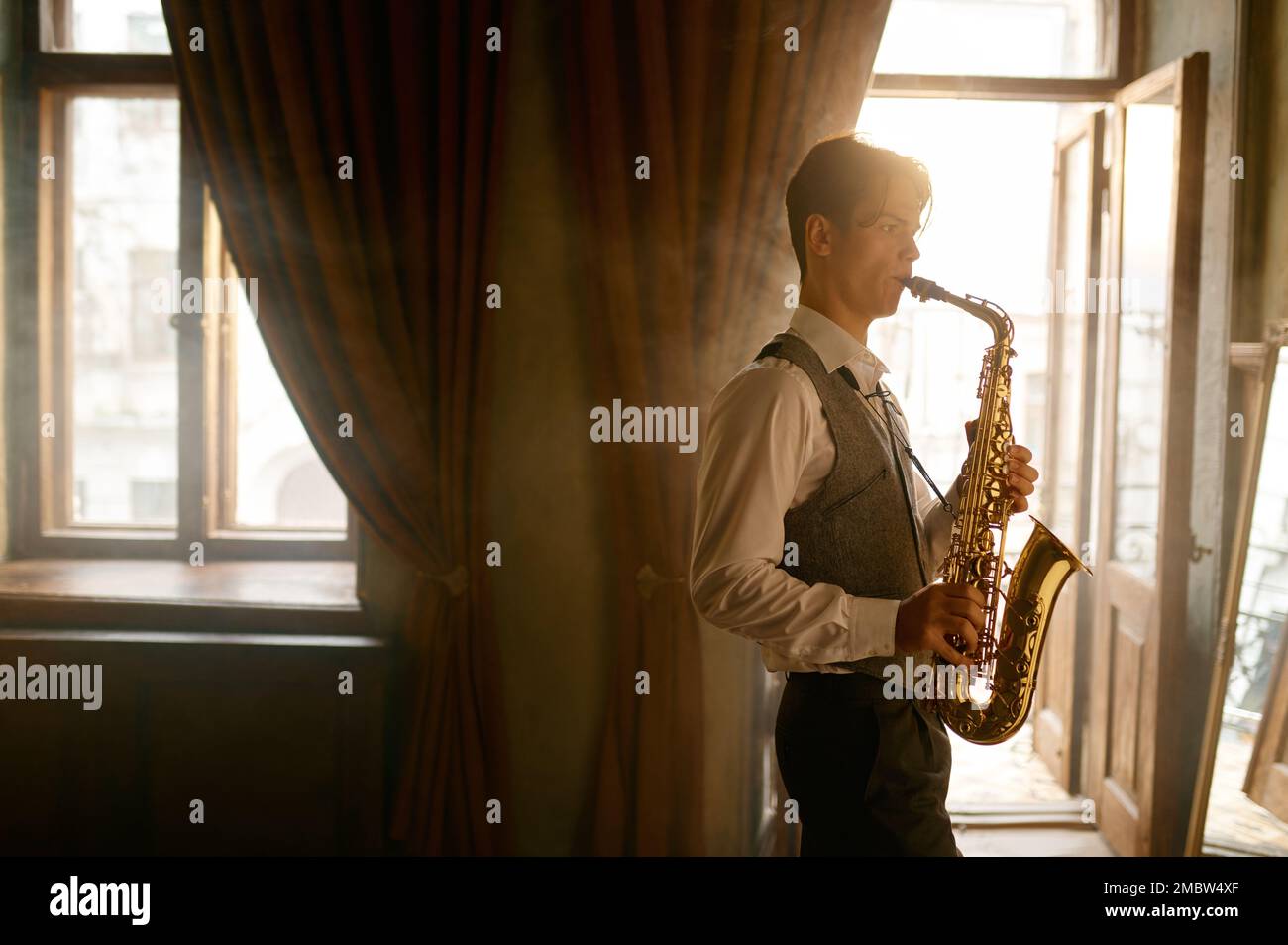 Giovane uomo elegante che suona il sassofono dell'alto in una stanza misteriosa Foto Stock