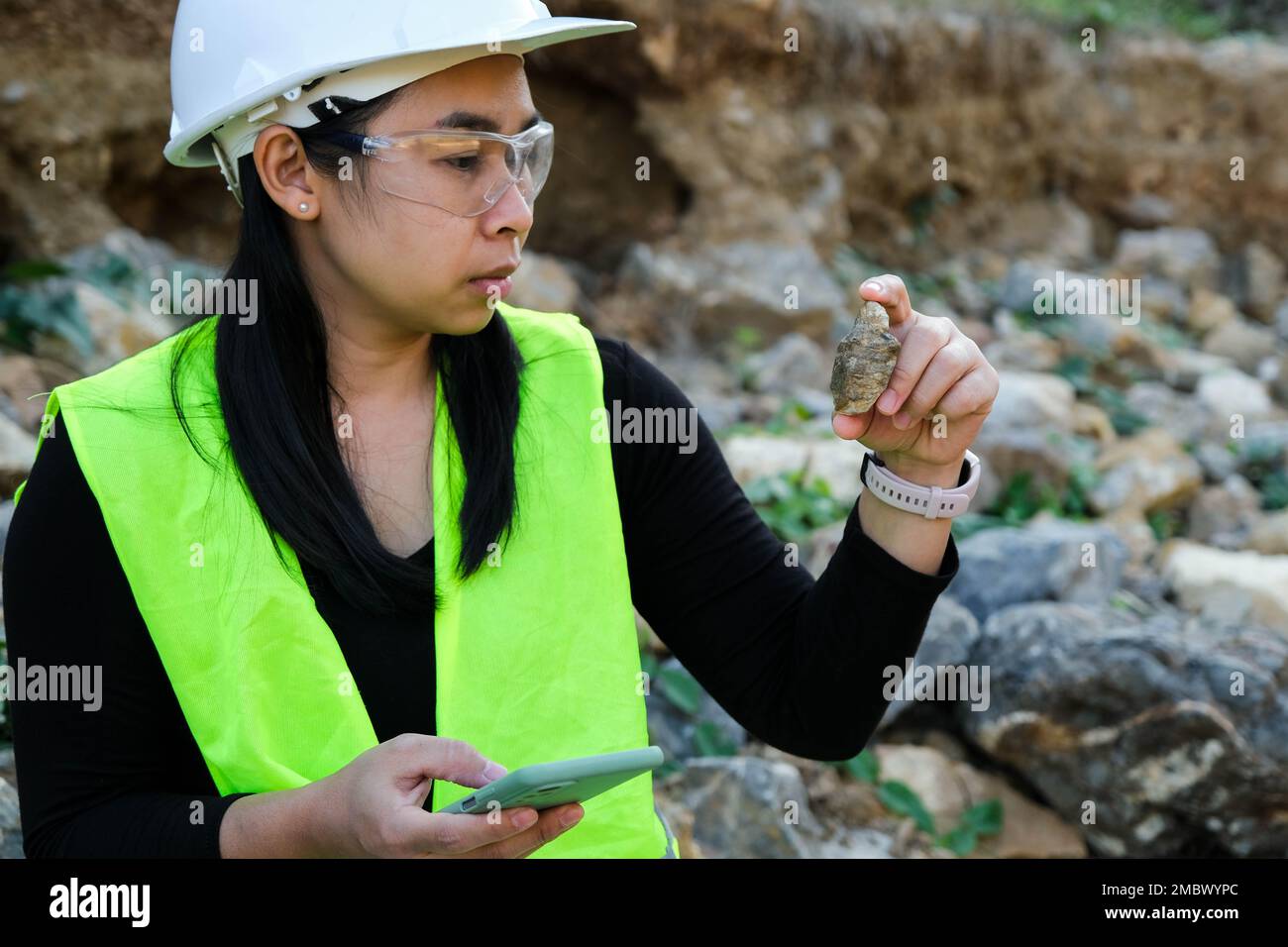 Geologo femminile che utilizza il telefono cellulare per registrare i dati di analisi di rocce o ghiaia. I ricercatori raccolgono campioni di materiali biologici. Ambientale ed e Foto Stock