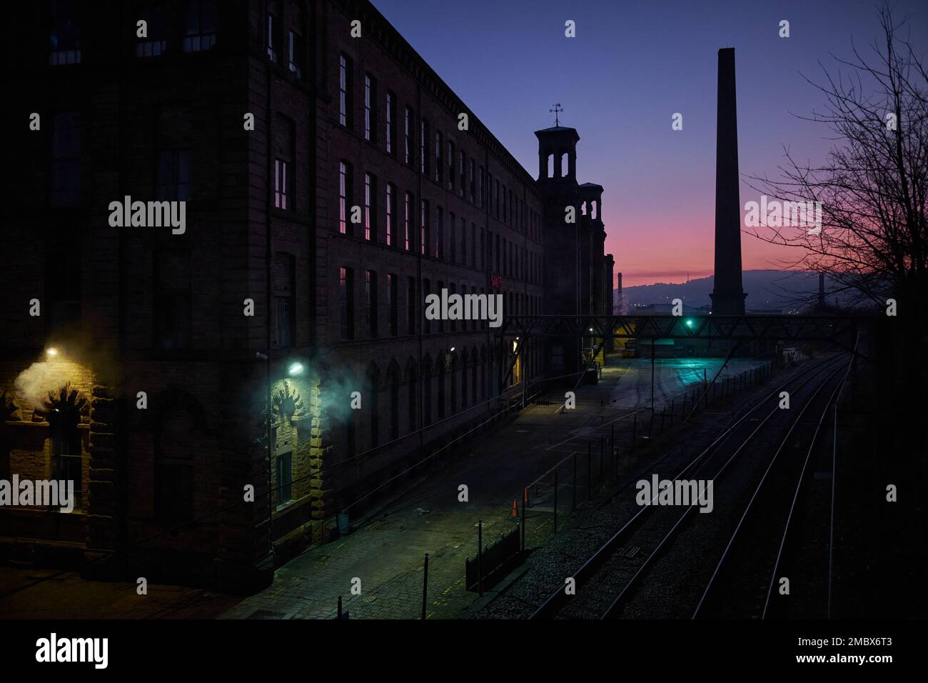 Luce rosa all'orizzonte all'alba su Salts Mills a Saltaire con luci all'aperto che si infrangono attraverso le ombre Foto Stock
