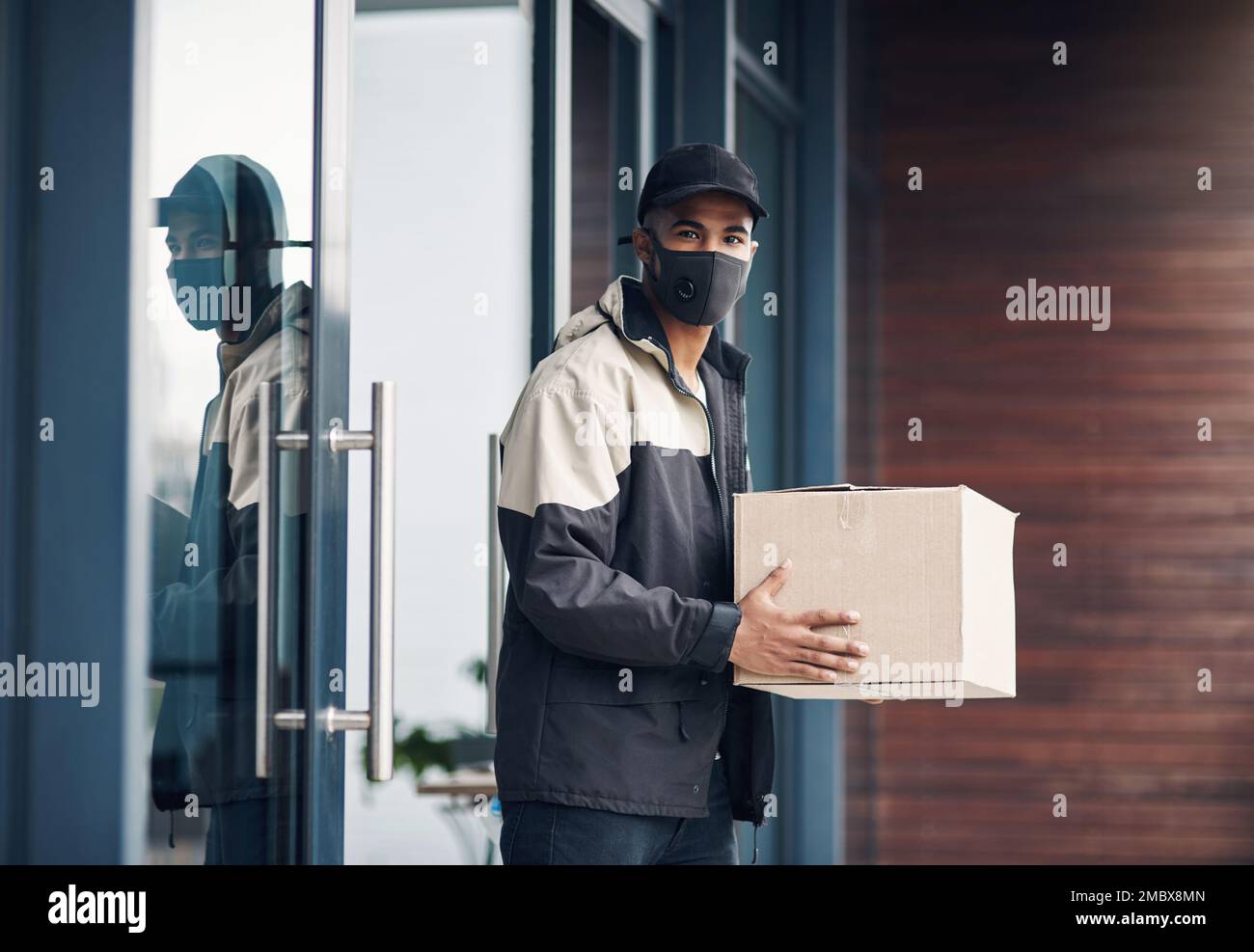 I corrieri professionali mantengono una distanza di sicurezza. un giovane mascherato che consegna un pacchetto in un luogo di residenza. Foto Stock