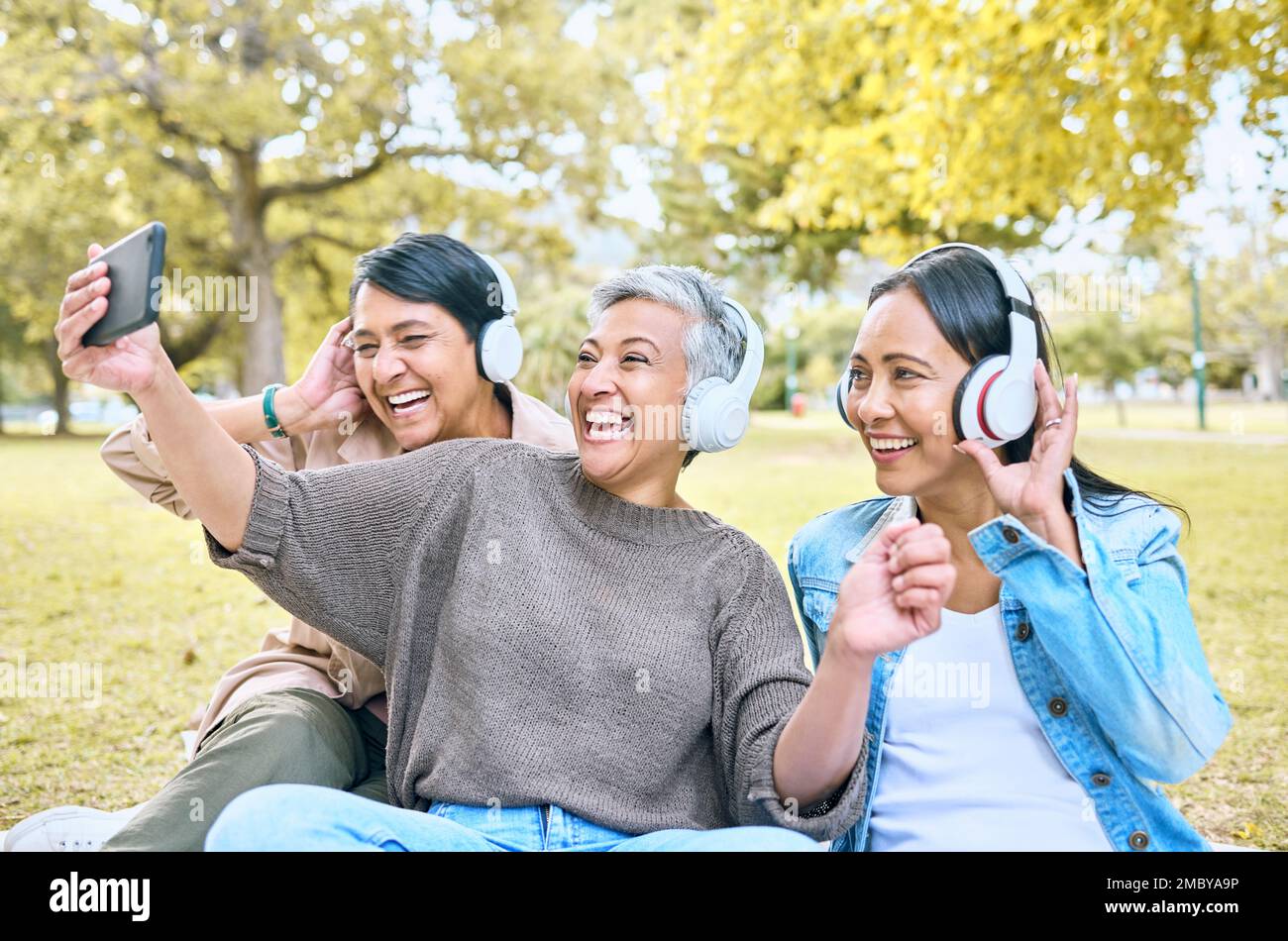 Cuffie, amici, selfie e donne al parco che scattano foto per i social media. Musica in streaming mobile, pensionamento e gruppo di donne anziane Foto Stock