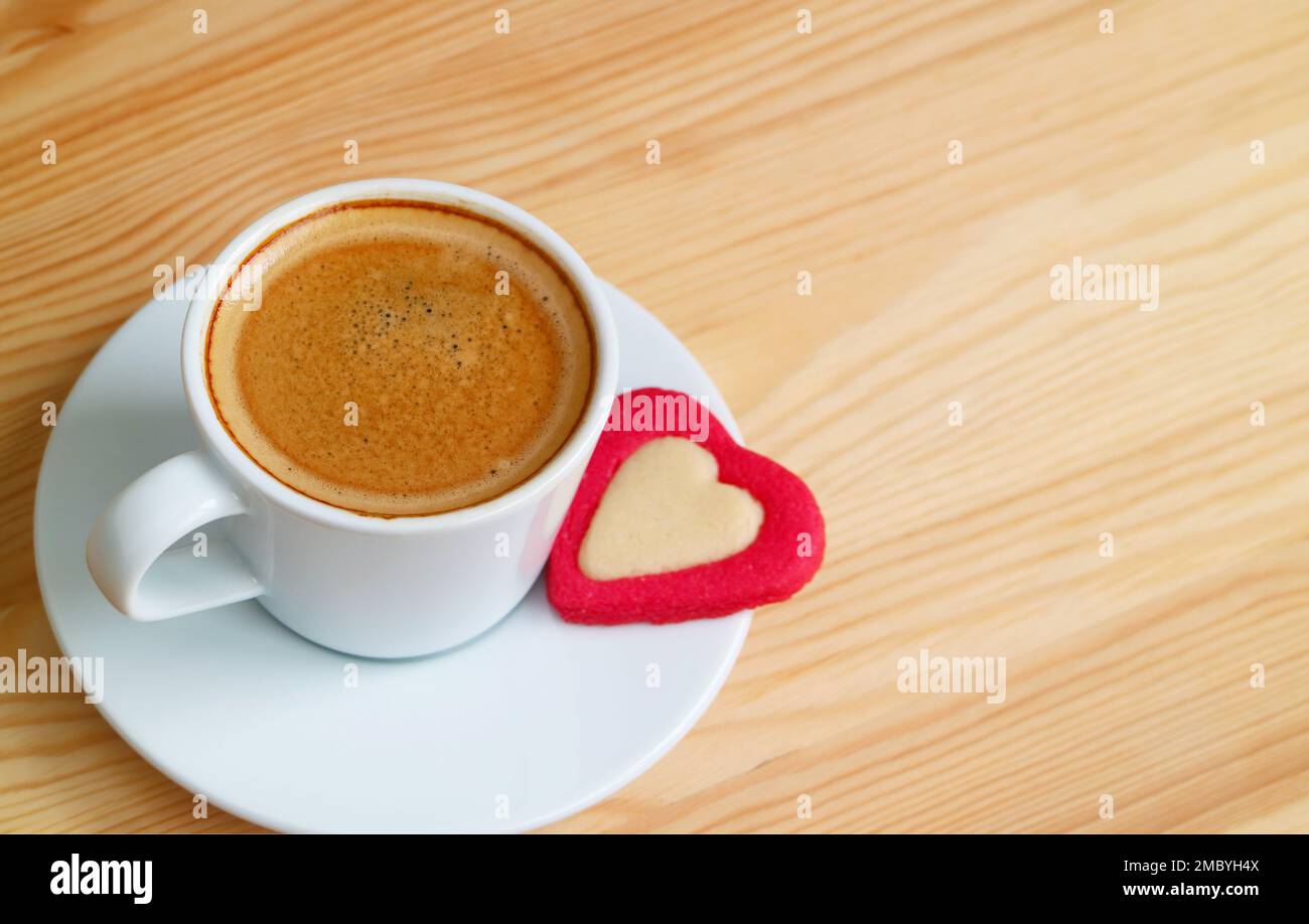 Tazza di caffè caldo schiumoso con un biscotto a forma di cuore su un tavolo di legno Foto Stock